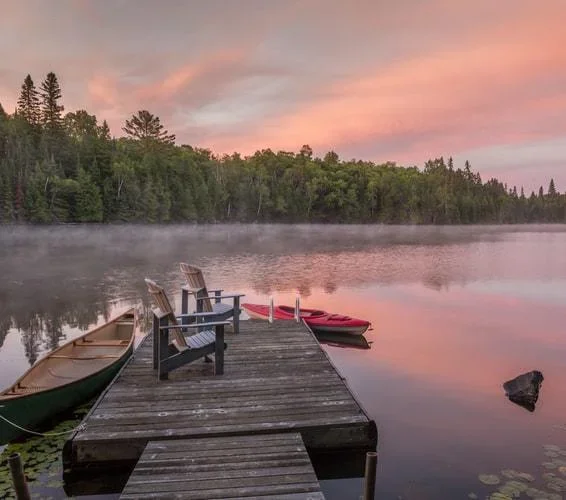 Rowboats on a dock sitting on top of the lake in Haliburton Highlands with a sunset beaming over the waters
