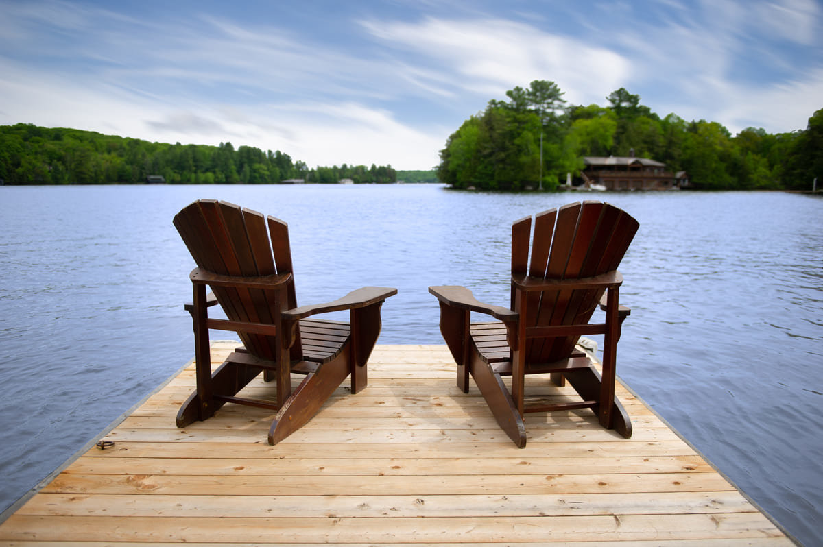 Two muskoka chairs sitting on a dock during the day time.