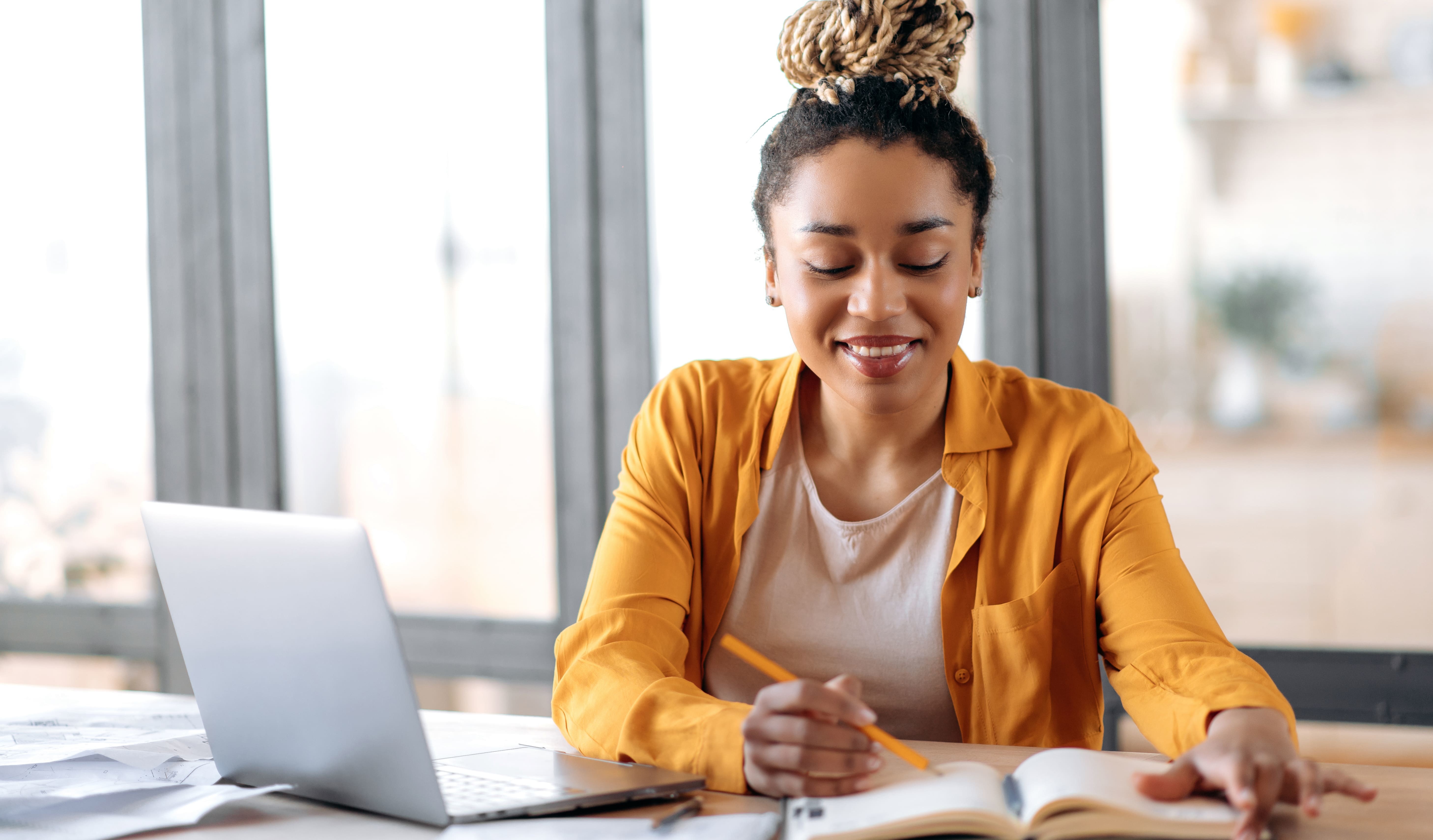 Closing a home remotely. A woman working on a laptop and writing in a journal.