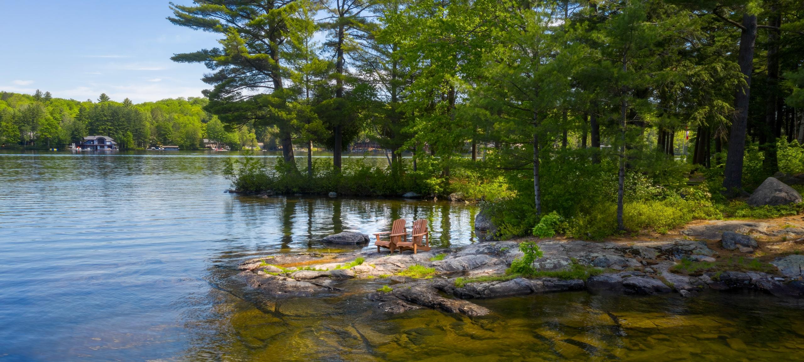 Two chairs on jutting rocks with lakefront cottages in background, Lake Rosseau